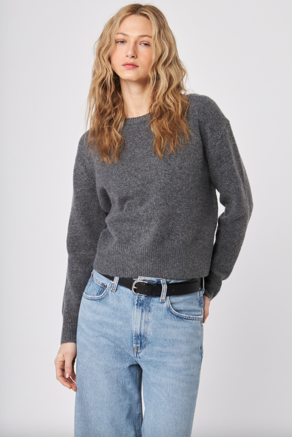 Woman wearing a gray sweater and blue jeans against a white background