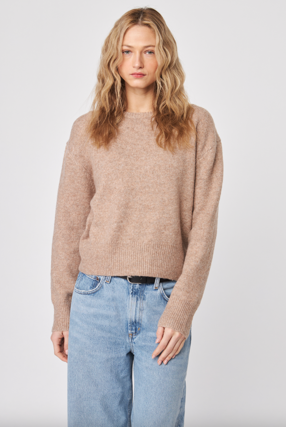 Woman wearing a beige sweater and light blue jeans against a white background
