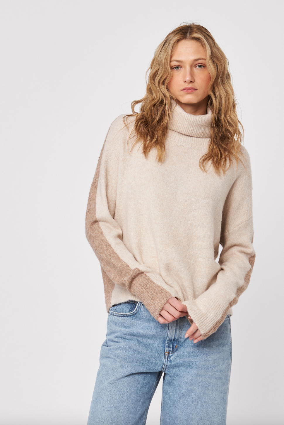 Woman wearing a beige sweater and blue jeans on a white background