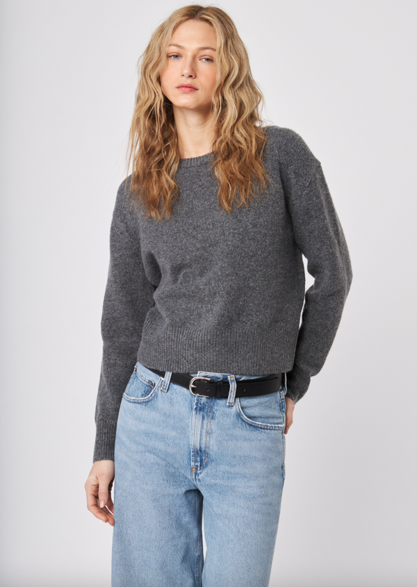 Woman wearing a gray sweater and blue jeans against a white background
