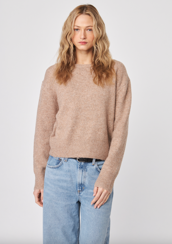 Woman wearing a beige sweater and light blue jeans against a white background