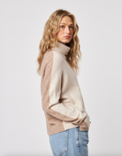 Woman wearing a two-tone sweater and jeans on a plain background