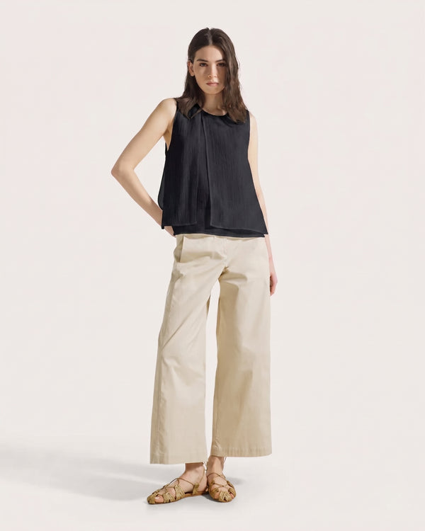 Woman wearing a black sleeveless top and beige wide-leg pants on a white background
